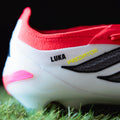 Close-up of a red and white sports shoe with 'Luka' decals on grass.