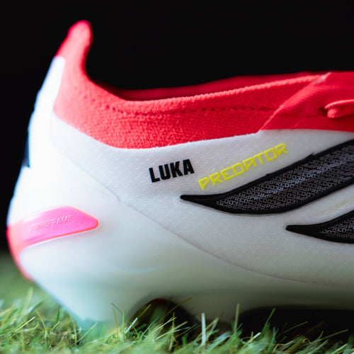 Close-up of a red and white sports shoe with 'Luka' decals on grass.