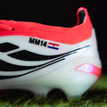 Close-up of a sports shoe with red top and white sole on grass showing custom decals 